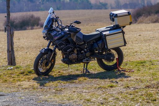 A parked Yamaha XT 1200 Z motorcycle with side cases on the edge of the meadow