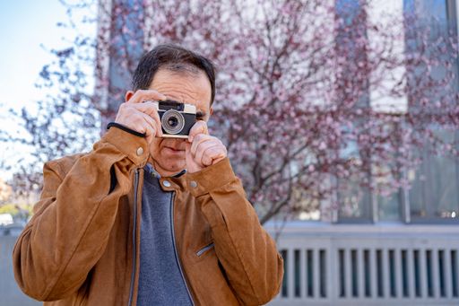 An older man is photographed while shooting with his old film camera.