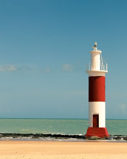 A lighthouse against a blue cloudy sky on a sunny day at a beach