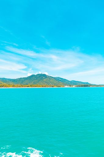 A vertical shot of a sea with forested mountains in the distance under a blue sky at daytime