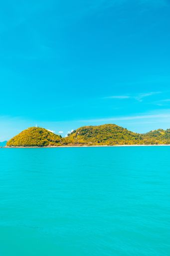 A vertical shot of a blue water sea with forested mountains in the distance under a blue sky