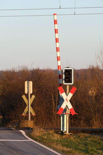 Open railroad crossing with a barrier and a traffic light. Transport and railway infrastructure. Vertical shot at sunset.