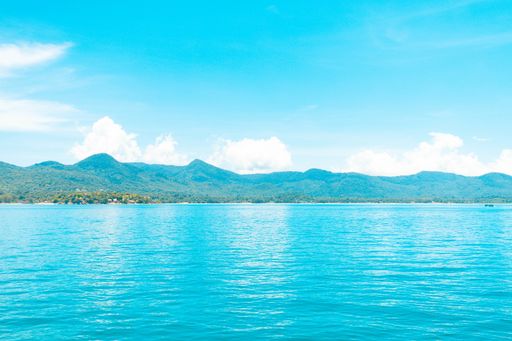 A beautiful shot of the blue water sea with forested mountains in the distance under a blue sky