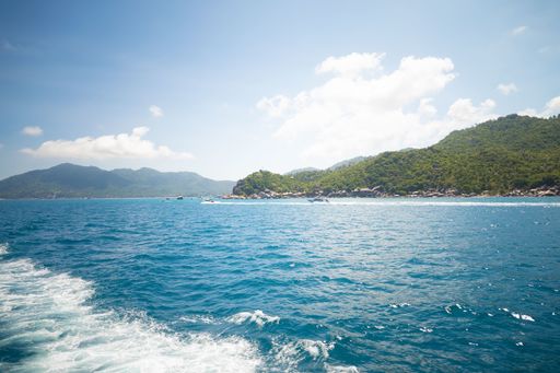 A beautiful shot of the sea with forested mountains in the distance under a blue cloudy sky