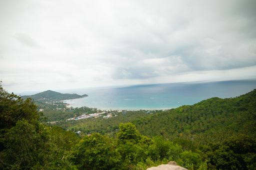 A high angle shot of hills covered in trees near the sea under a cloudy sky