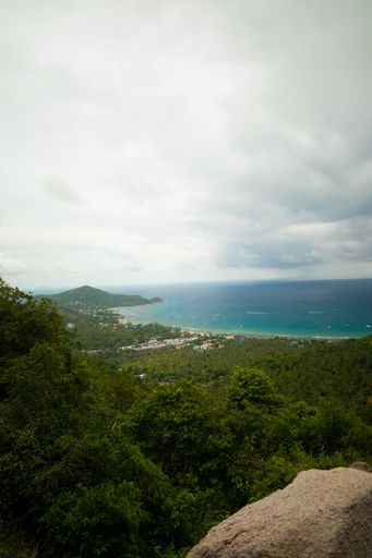 A vertical shot of hills covered in trees near the sea under a cloudy sky