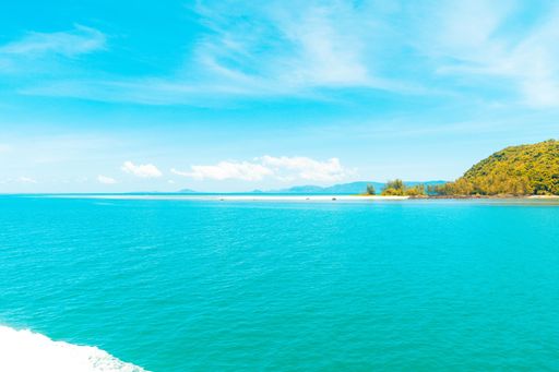 A beautiful shot of the sea with a hill covered in trees under a blue sky at daytime
