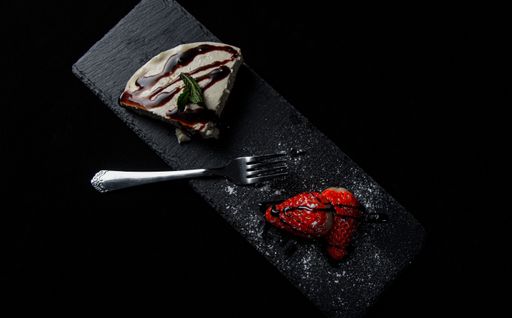 A top view of a delicious slice of cake next to strawberries on a plate isolated on a black background