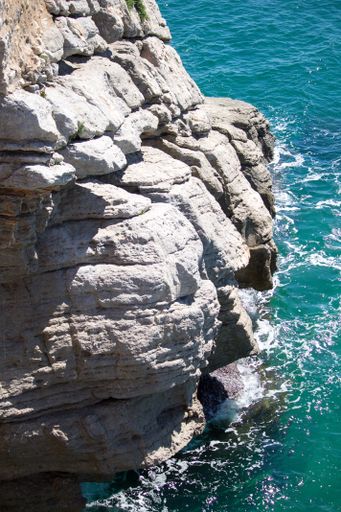 A vertical shot of a rocky cliff next to a beautiful blue sea during daylight