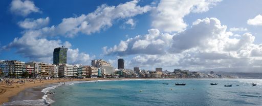 A panoramic view of a sandy beach and tourists under a cloudy sky in Las Palmas de Gran Canaria, Spain