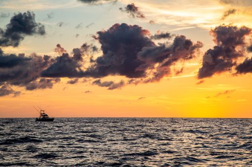 The beautiful ocean with a small boat sailing through it, colored by a yellow sunset