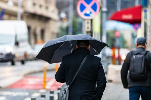 Some people with umbrellas on a street on a rainy day in Bucharest, Romania