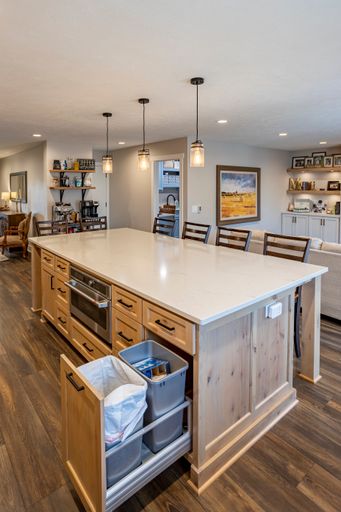 A vertical shot of a large white kitchen island with a trash drawer in a beautiful room interior