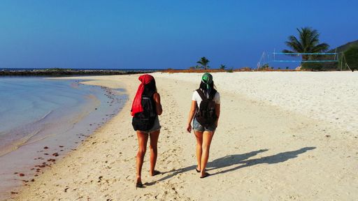 A backshot of two Caucasian females with backpacks walking on the seashore beach, Koh Samui, Thailand