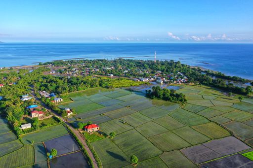 An aerial view of rice fields house buildings and the sea in Pota, Flores, Indonesia