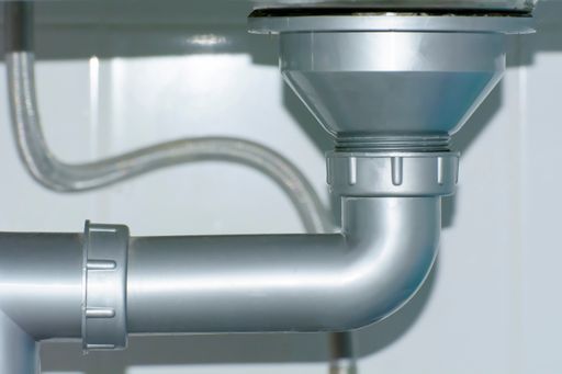 A closeup of a drainage pipe under a kitchen sink