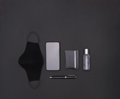 A top view of a mask, smartphone, cardholder, hand sanitizer, and ballpen on a black background