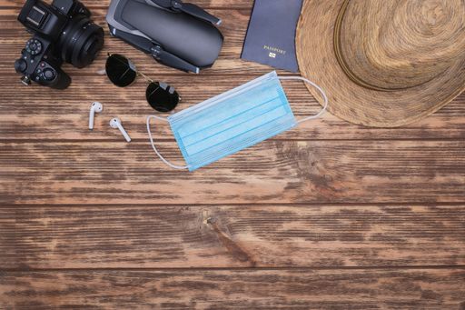 A top view of a camera, drone, sunglasses, ear pads, mask, passport, and a hat on a wooden background