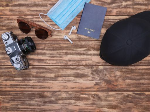 A top view of a camera, sunglasses, mask, passport, ear pads and hat on a wooden background