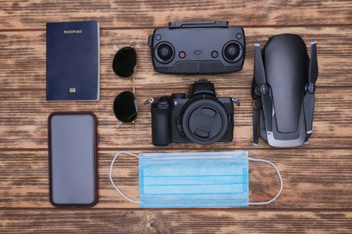 A top view shot of passport, sunglasses, smartphone, mask, camera, drone, and drone controller on a wooden background