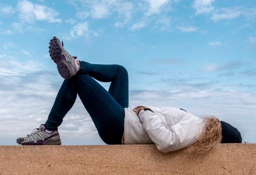 A shot of a Caucasian female lying down on a concrete wall, looking at the blue cloudy sky