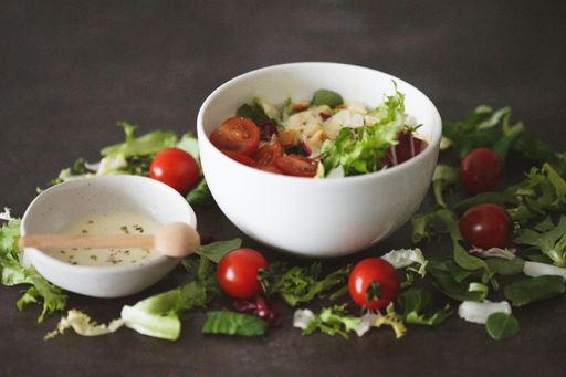 A closeup shot of a salad and a sauce in a white bowl surrounded by vegetables