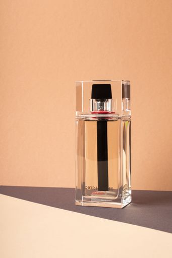 A minimalist shot of a Dior Homme sport perfume bottle on a light orange background