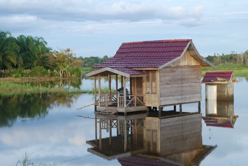 A landscape shot of a small log cabin on a lake under the peaceful sky