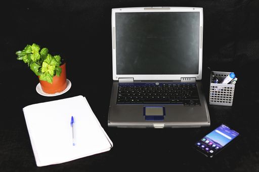 A closeup shot of a laptop, phone, plant, notebook and pen box on black background