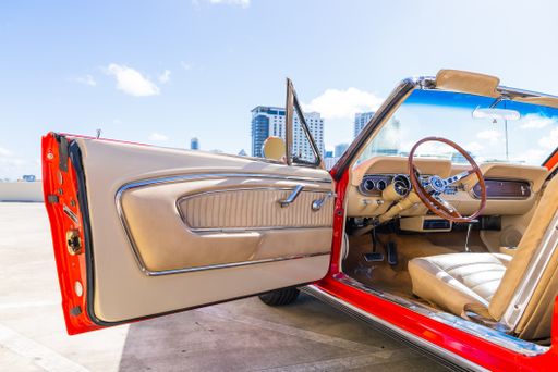 A red 1966 convertible Ford Mustang with an open door showing the beige leather interior