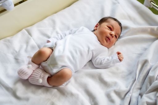 A photo of a newborn boy in the hospital, with a white bodysuit lying in the crib