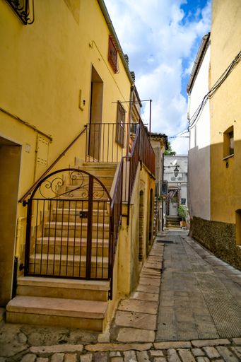 A vertical photo of a narrow street and classic buildings in Lavello, an old town in Basilicata region, Italy