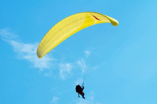 A paraglider with yellow wing in mid air against a clear blue sky