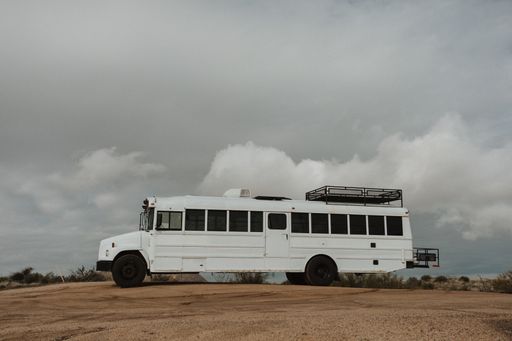 A horizontal shot of a white bus from the side in a dry field during daylight