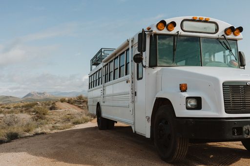 A horizontal shot of a white bus from the front in a dry field during daylight