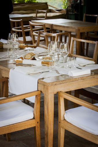 A vertical shot of wooden chairs and table with napkins, glasses, and bread on it in a restaurant