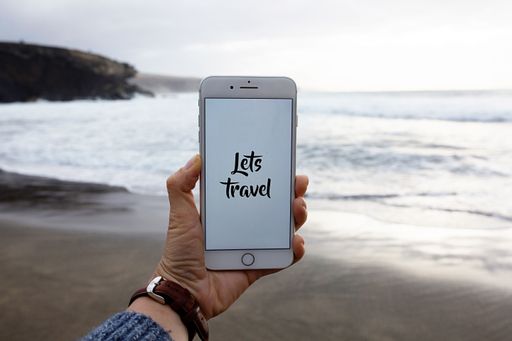 A person holding a phone with let's travel text and a blurred beach in the background