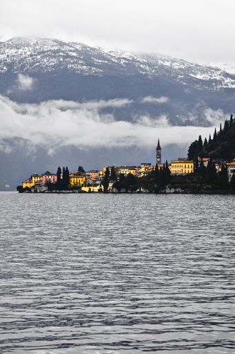 A vertical shot of a sea with buildings near the mountain in the distance under a cloudy sky