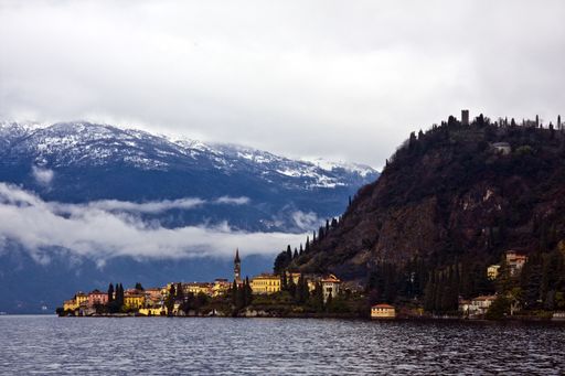 A beautiful shot of the sea with buildings near the mountains in the distance under a cloudy sky
