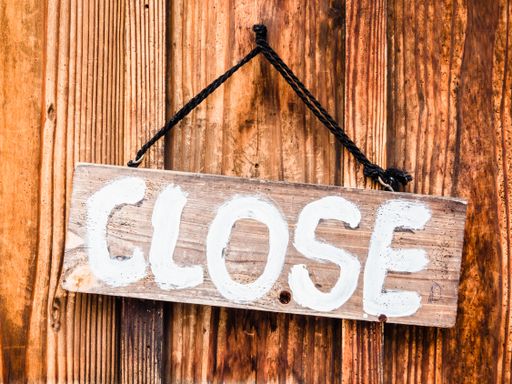 A wooden sign with [CLOSE] written on it hanging with ropes from the door