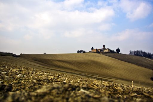 A beautiful shot of a dry grassy field with a house on top of the hill under a blue cloudy sky