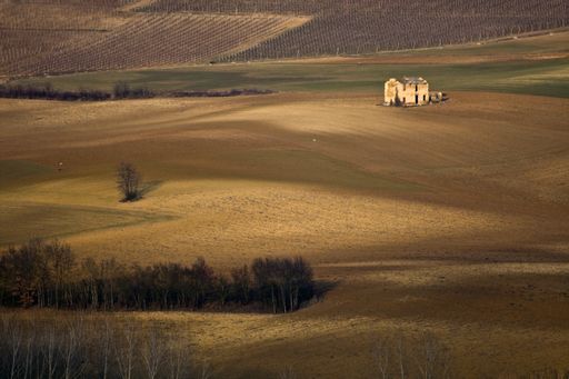 A high angle shot of an abandoned building in the middle of dry grassy fields at daytime