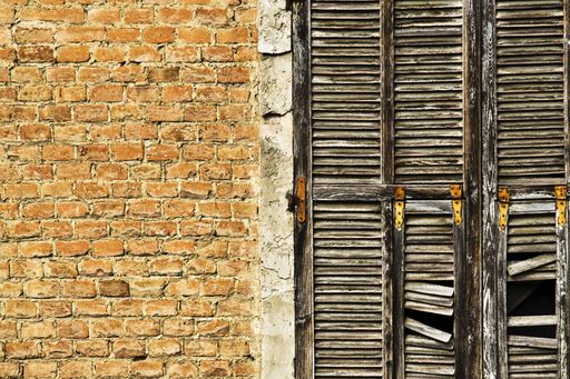 A close shot of a brick house with a broken wooden window frame at daytime