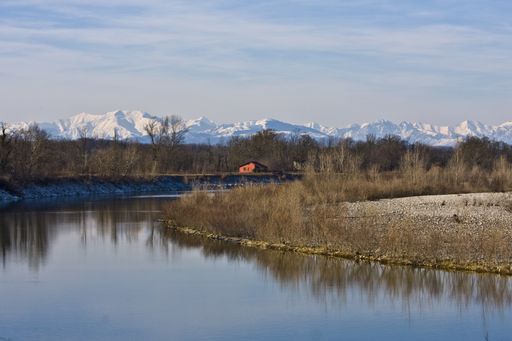 A beautiful shot of a river in the middle of shores and leafless trees with a house in the distance