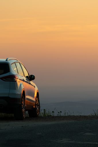 A vertical shot of a white car parked on the side of the road at sunset