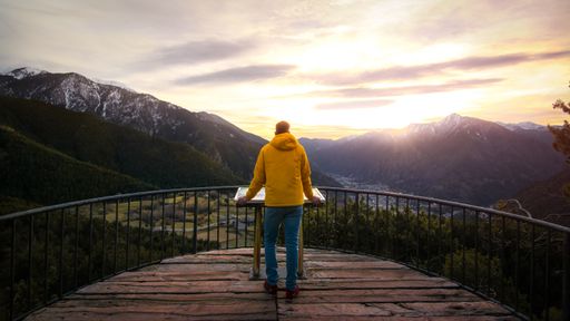 A closeup shot of a male standing on a wooden balcony with mountains on the background
