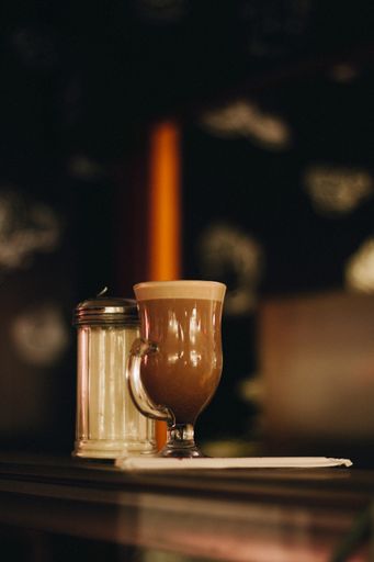 A vertical selective focus shot of a glass of coffee with sugar on the side on a table