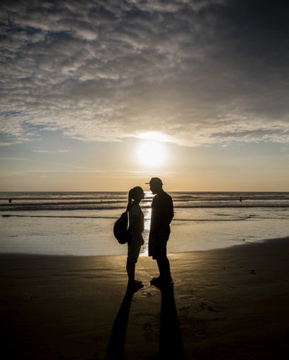 The silhouettes of a couple standing on the coastline under the evening sky