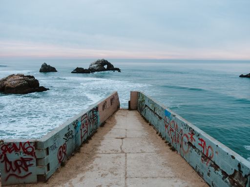 A beautiful shot of a pathway towards the sea with rocks in the distance under a cloudy sky