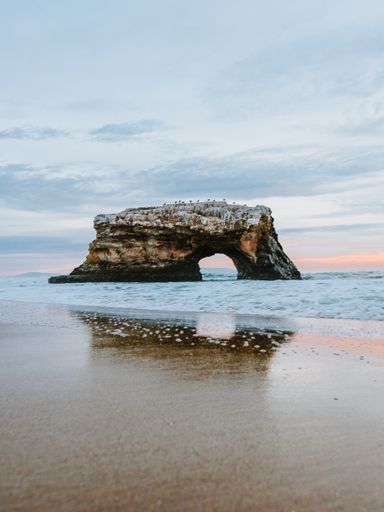 A vertical shot of a rock formation in the water near the shore under a cloudy sky